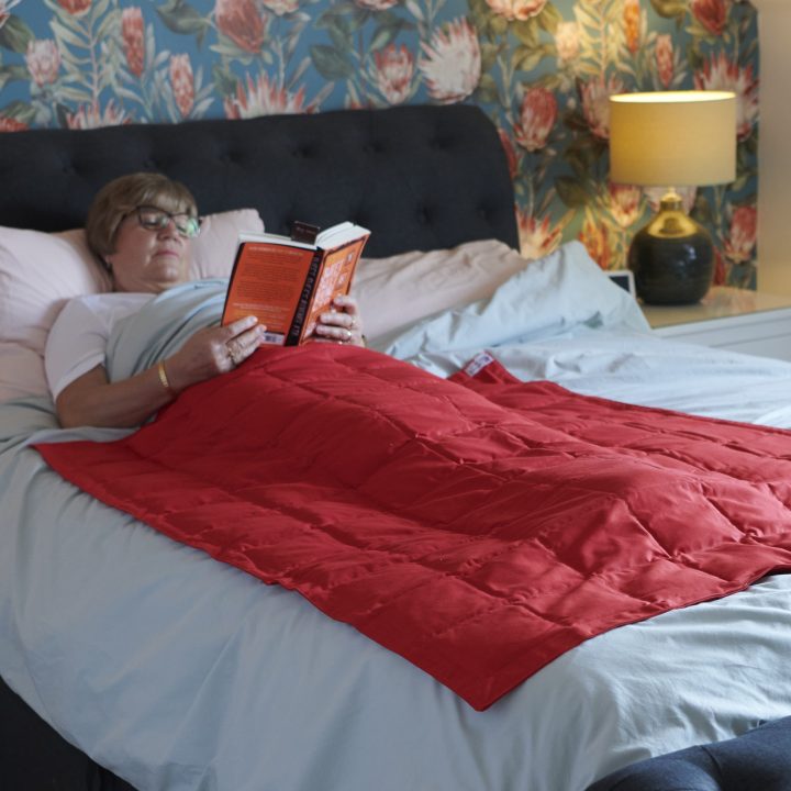 Woman reading book under red weighted blanket